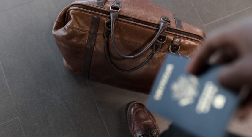homme qui tient son passeport et à un sac de voyage à ses pieds